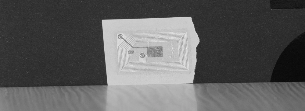 Close-up of a flexible RFID inlay printed on paper. The tag shows the extended conductive antenna and the chip, illustrating the internal structure essential for tracking systems