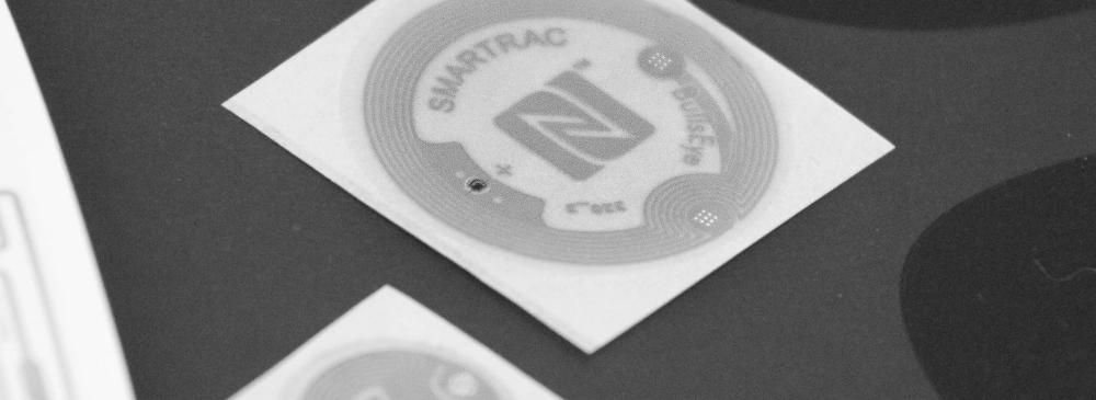 Smartrac BullsEye round adhesive NFC RFID (Radio Frequency Identification) inlay, illustrating the circular antenna design and the positioning of the microchip. An excellent resource for NFC hardware in tracking and identification systems.