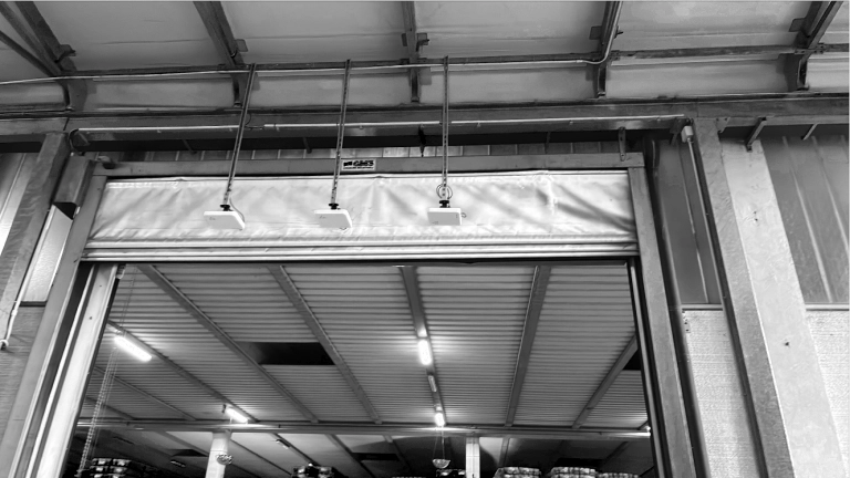 Warehouse loading bay with a linear RFID antenna array installed above the door. The connection cables and metal mounting brackets show the integration of the passive RFID tracking system into the logistics infrastructure.