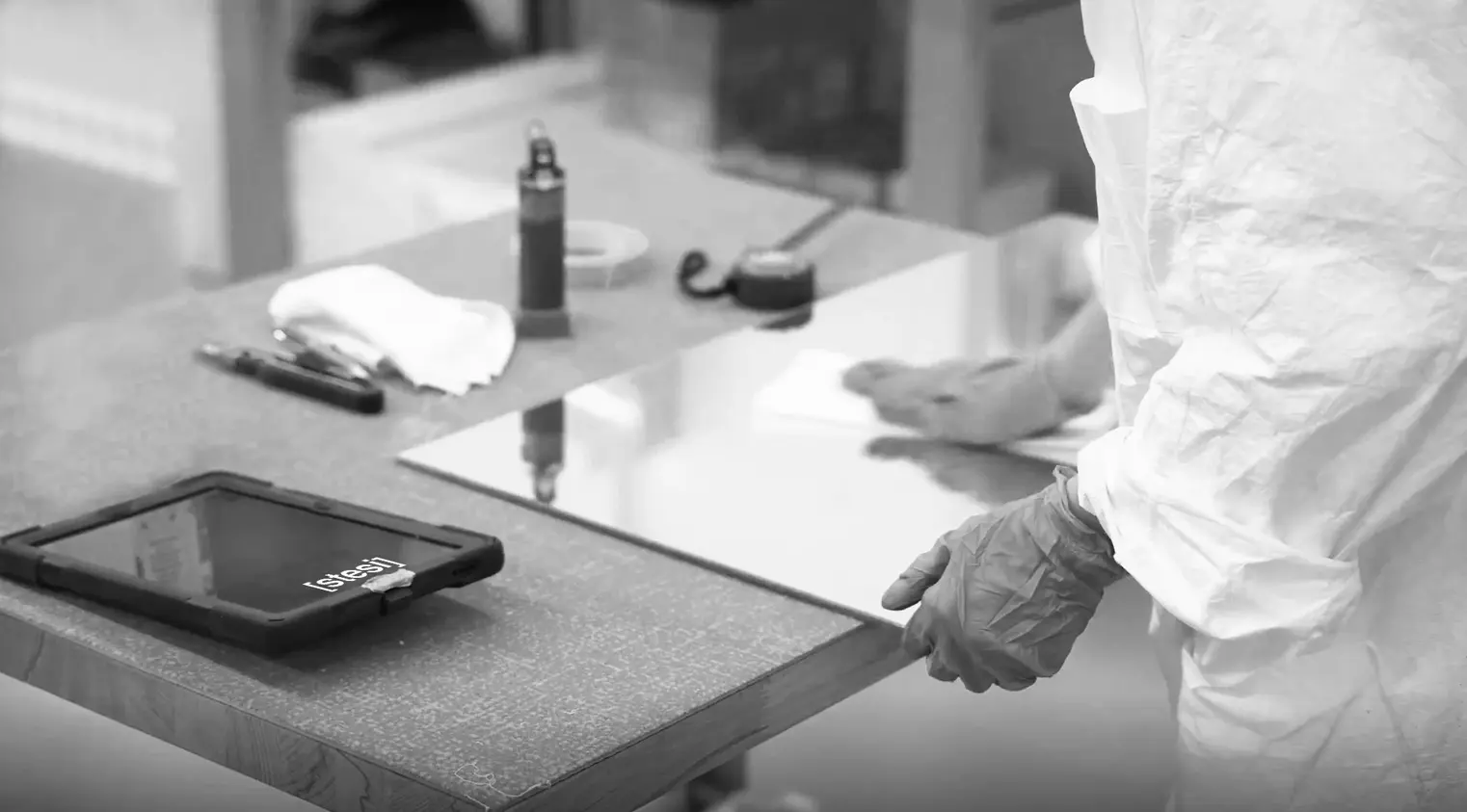 A Samo operator wearing gloves and a lab coat polishing a mirror component for bathroom furniture, with a Stesi WMS software terminal nearby