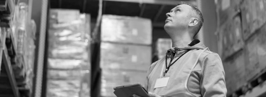 The modern warehouse: a warehouse worker looking up whilst holding a tablet industrial terminal